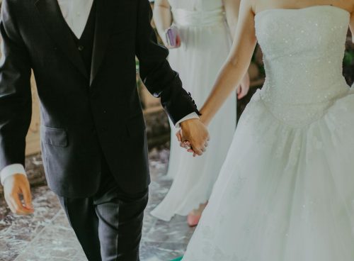 Woman Wearing White Wedding Gown Holding Hands With Man While Walking