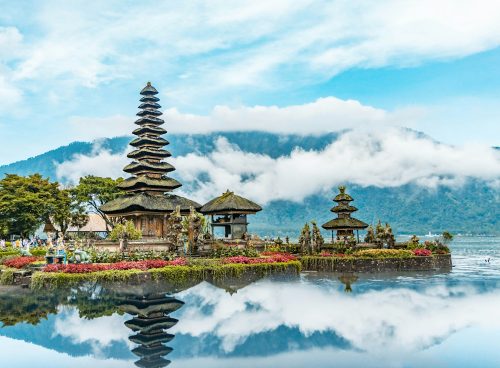 brown and green temple near body of water under blue and white cloudy sky during daytime
