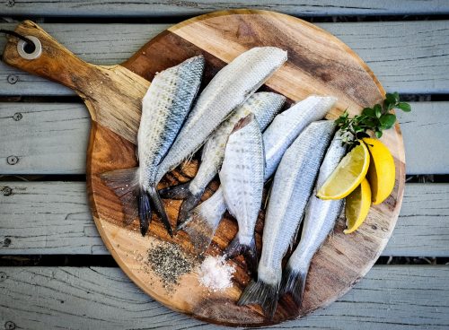 headless fishes with sliced of lemons on brown wooden chopping board