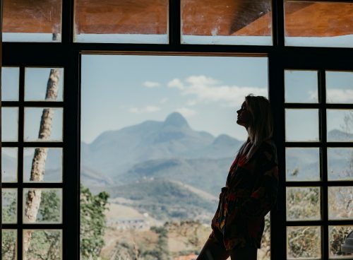 woman in red and black plaid dress shirt standing on window looking at mountains during daytime