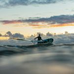 silhouette of man riding on blue kayak on sea during sunset