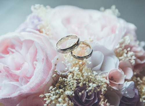 gold-colored bridal ring set on pink rose flower bouquet