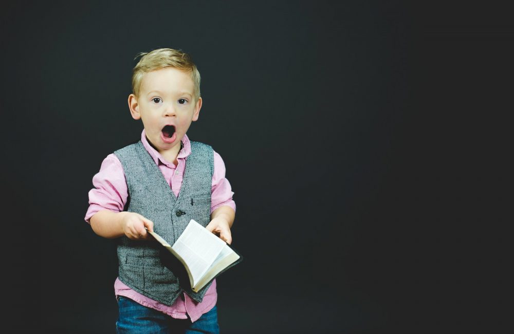 boy wearing gray vest and pink dress shirt holding book