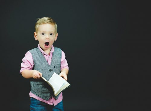 boy wearing gray vest and pink dress shirt holding book