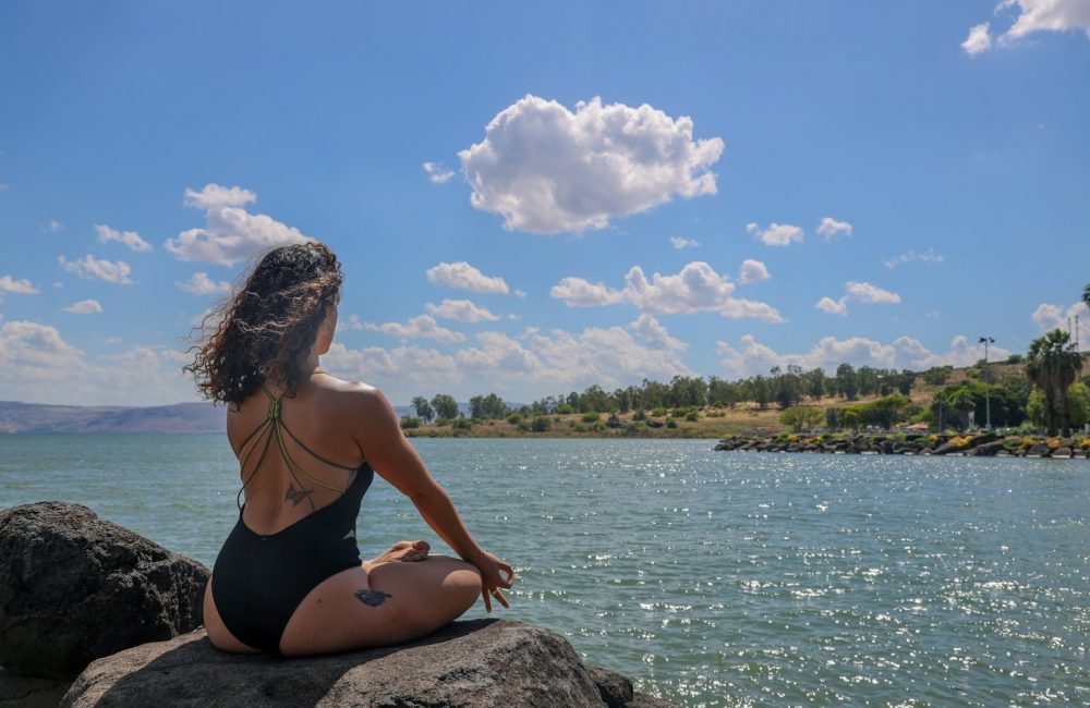 woman in black bikini sitting on rock near body of water during daytime