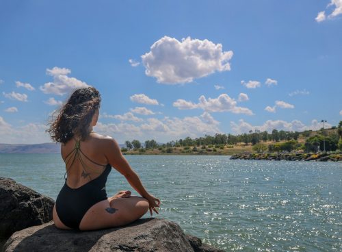 woman in black bikini sitting on rock near body of water during daytime