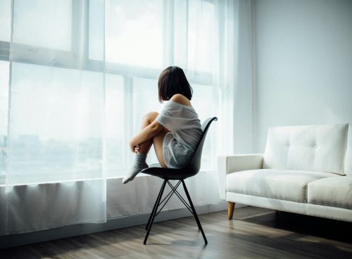 woman sitting on black chair in front of glass-panel window with white curtains