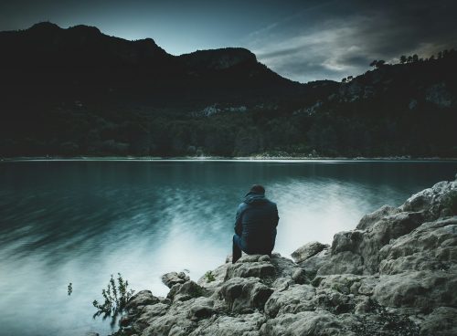 a man sits on a rock staring across a lake at dusk