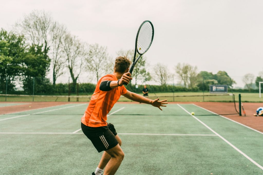 15 Sports and Exercises that Promote Height Growth in Teenagers 14 man in orange shirt and black shorts holding black and white tennis racket