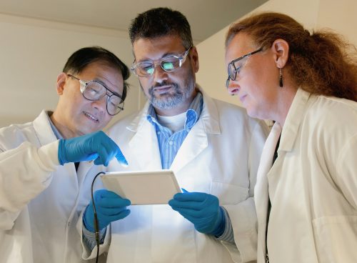 three people in lab coats looking at a tablet