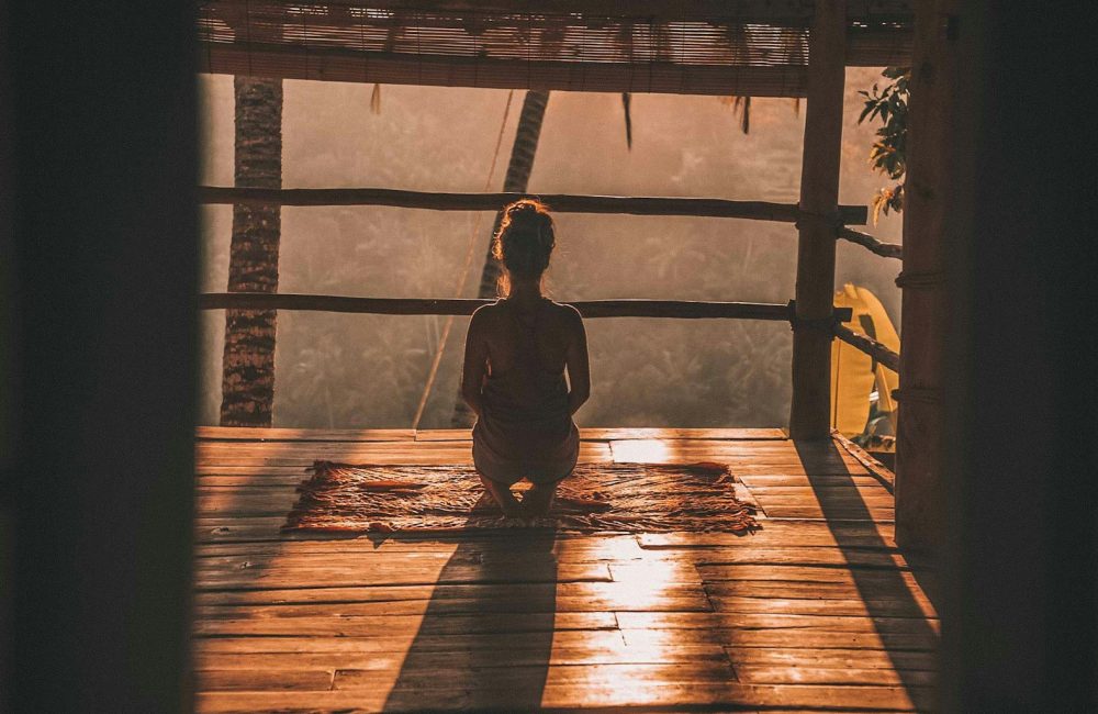 woman meditating on floor with overlooking view of trees