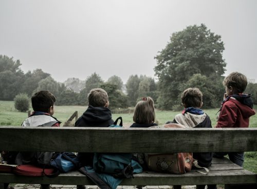 five children sitting on bench front of trees