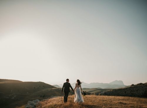 a bride and groom walking on a hill