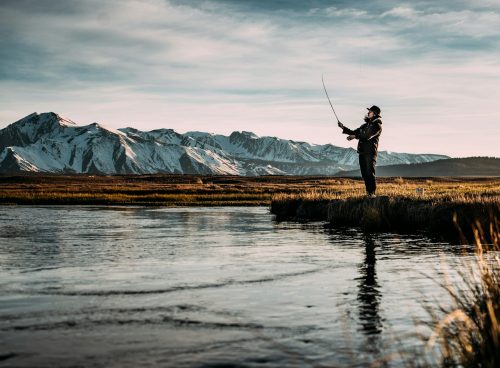 landscape photo of man fishing on river near mountain alps
