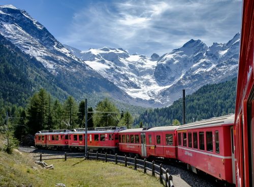 red and white train near green field viewing mountain and green trees