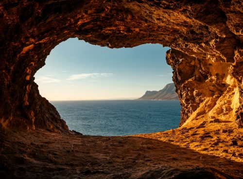 brown cave near body of water during daytime