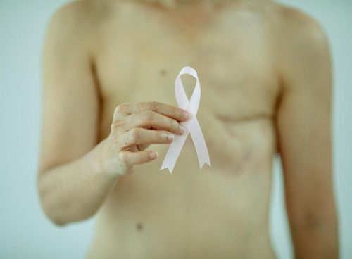 Crop anonymous female with breast cancer showing ribbon on white background of studio