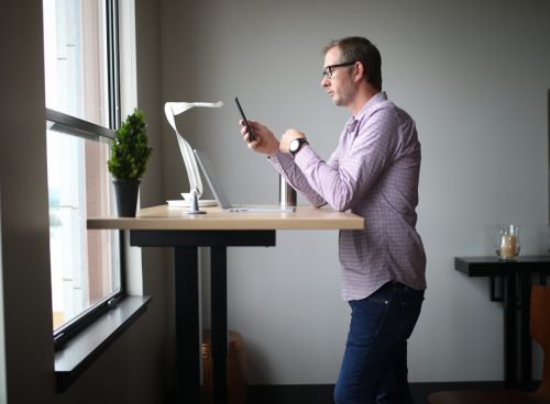 man in pink dress shirt and blue denim jeans standing beside brown wooden table