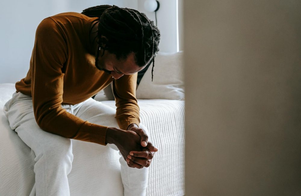 Desperate black man sitting on bed in deep thoughts