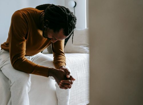 Desperate black man sitting on bed in deep thoughts