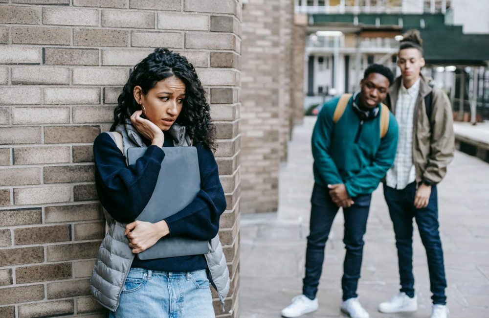 Latin American woman leaning on brick wall while hiding from multiracial classmates in college