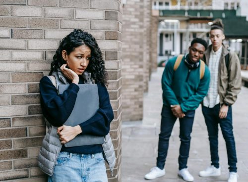 Latin American woman leaning on brick wall while hiding from multiracial classmates in college