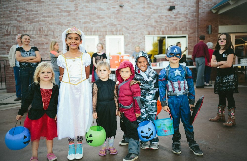 children standing while holding Jack 'o lantern and wearing costume