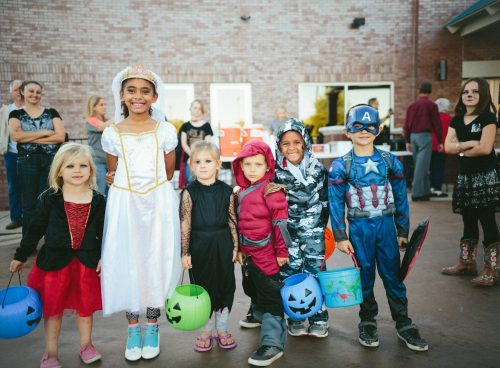 children standing while holding Jack 'o lantern and wearing costume