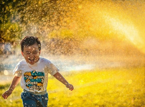 a young boy running through a sprinkle of water