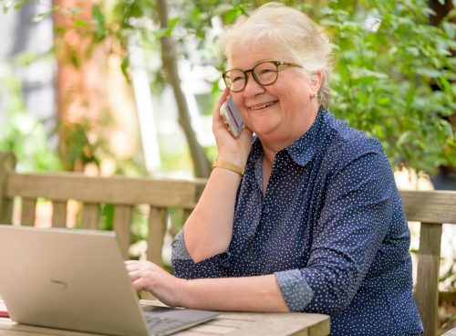 a woman on her phone while sitting at a table with a laptop