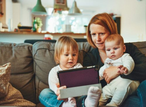two babies and woman sitting on sofa while holding baby and watching on tablet
