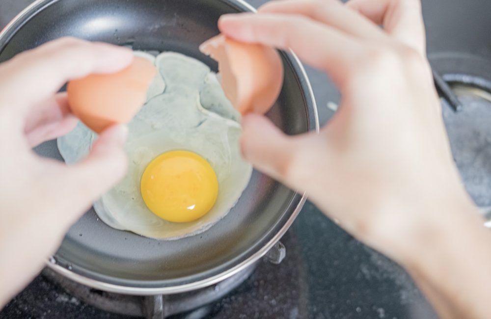 person holding black frying pan with egg