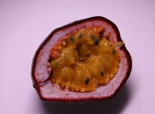 a cut open passion fruit on a pink surface