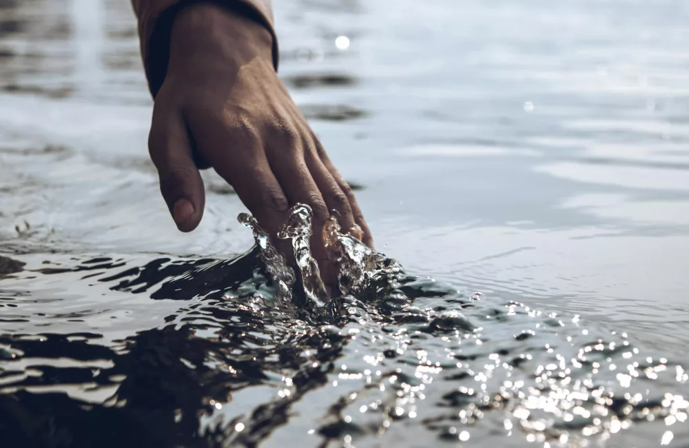 A serene close-up of a hand gently touching a sparkling water surface under daylight.