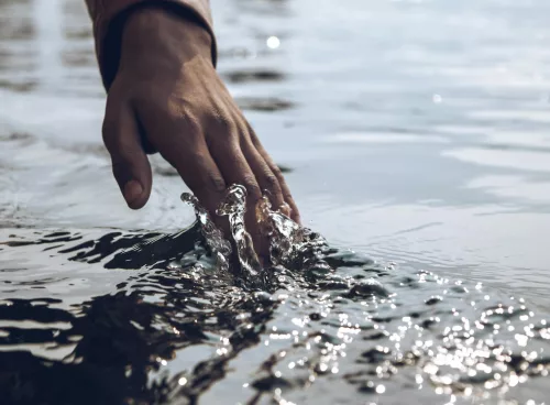 A serene close-up of a hand gently touching a sparkling water surface under daylight.