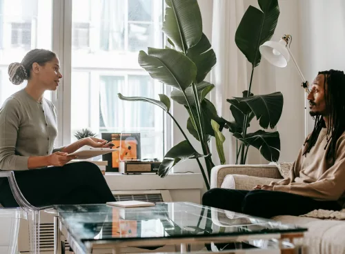 Side view of professional female African American therapist sitting in front of black male patient during psychotherapy session in office
