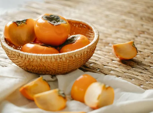 A wicker basket filled with ripe persimmons on a textured surface, symbolizing natural and healthy eating.