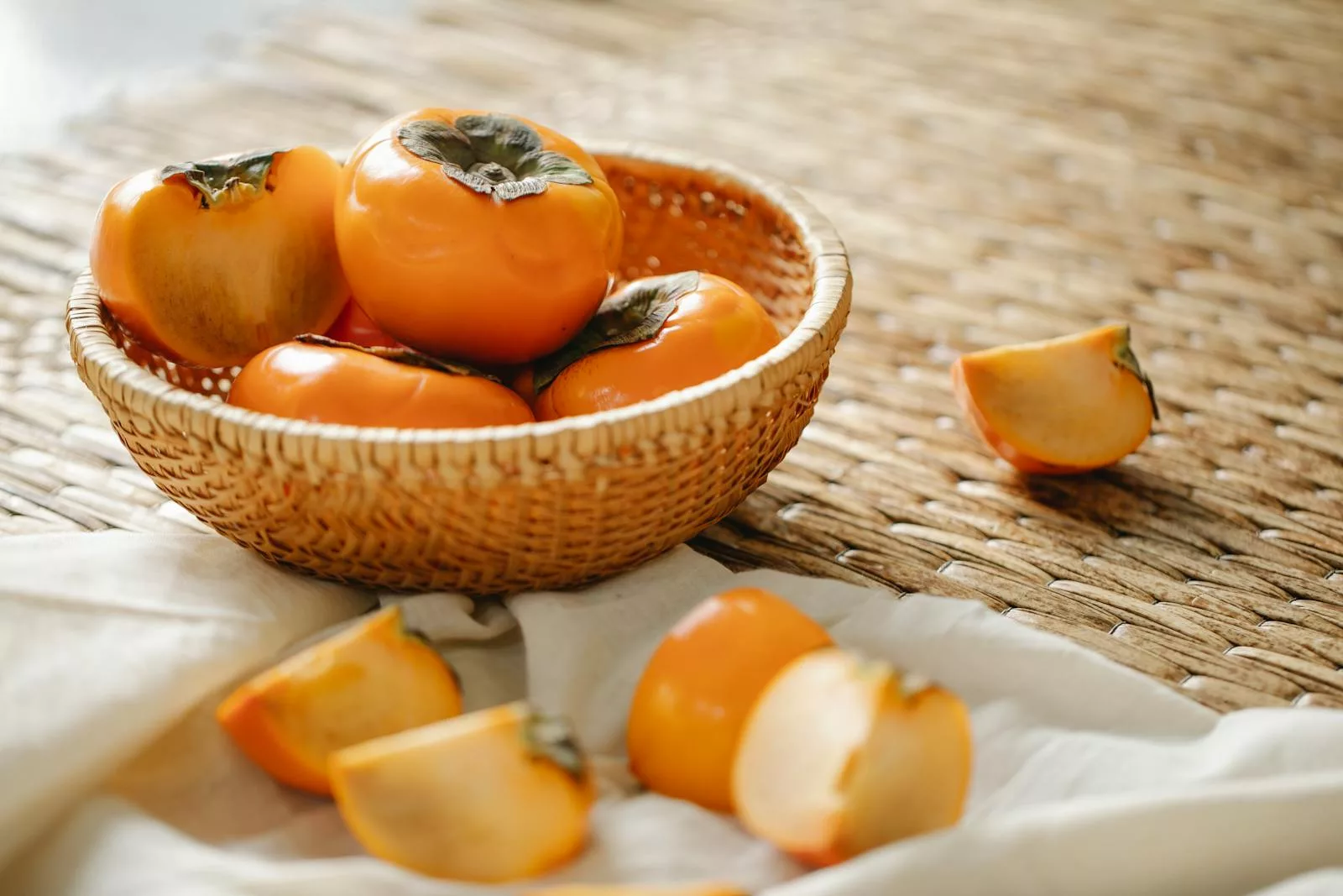 15 Surprising Health Benefits of Persimmons for Women 1 A wicker basket filled with ripe persimmons on a textured surface, symbolizing natural and healthy eating.
