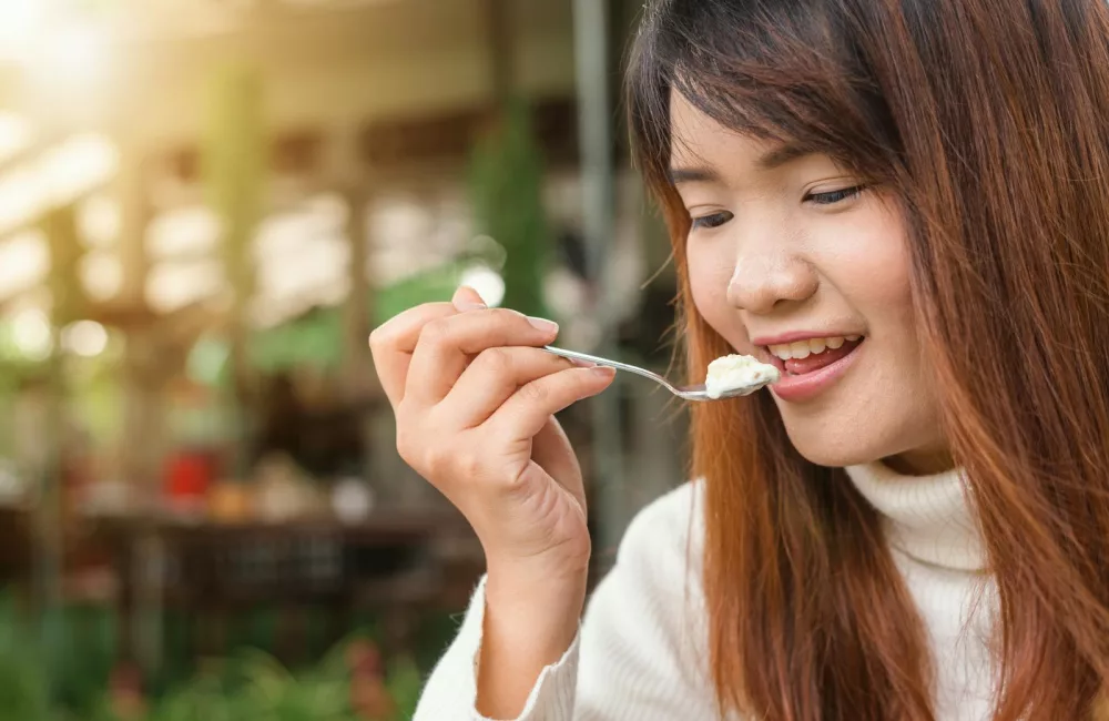 Happy woman enjoying a creamy dessert in a sunlit outdoor setting.