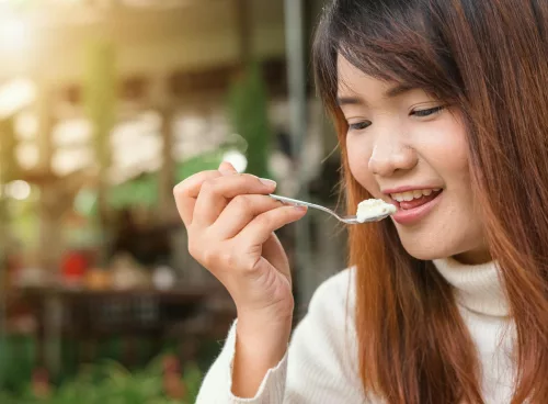 Happy woman enjoying a creamy dessert in a sunlit outdoor setting.