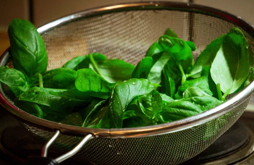 a colander filled with green leaves on top of a stove