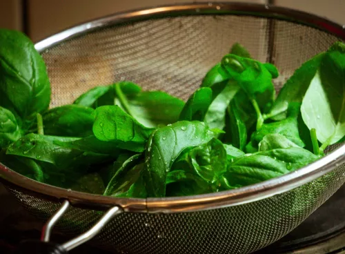 a colander filled with green leaves on top of a stove