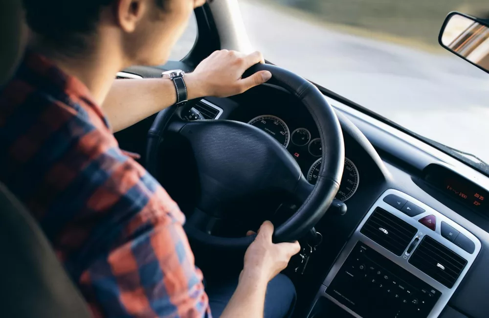 Close-up view of a man driving a modern car, showing dashboard and steering details.